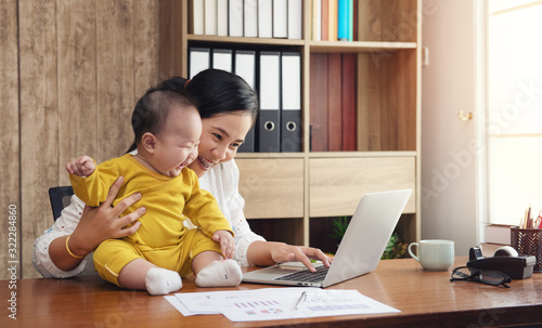 working asian mother and baby boy and laptop computer at home office