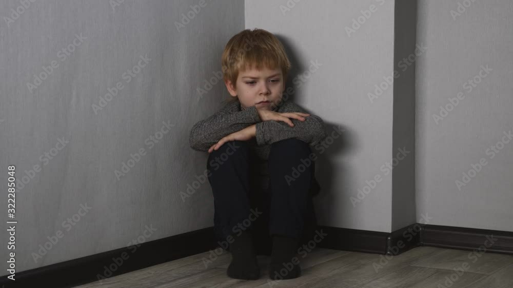 A scared, lonely blond boy sits on the floor in the corner of the room. A scared, lonely blond boy sits on the floor in the corner of the room.