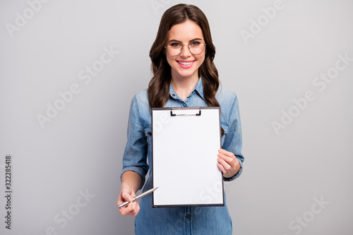 Here. Photo of beautiful wavy business lady hold clipboard showing contract space for signing up details wear specs casual jeans denim shirt isolated grey color background photo