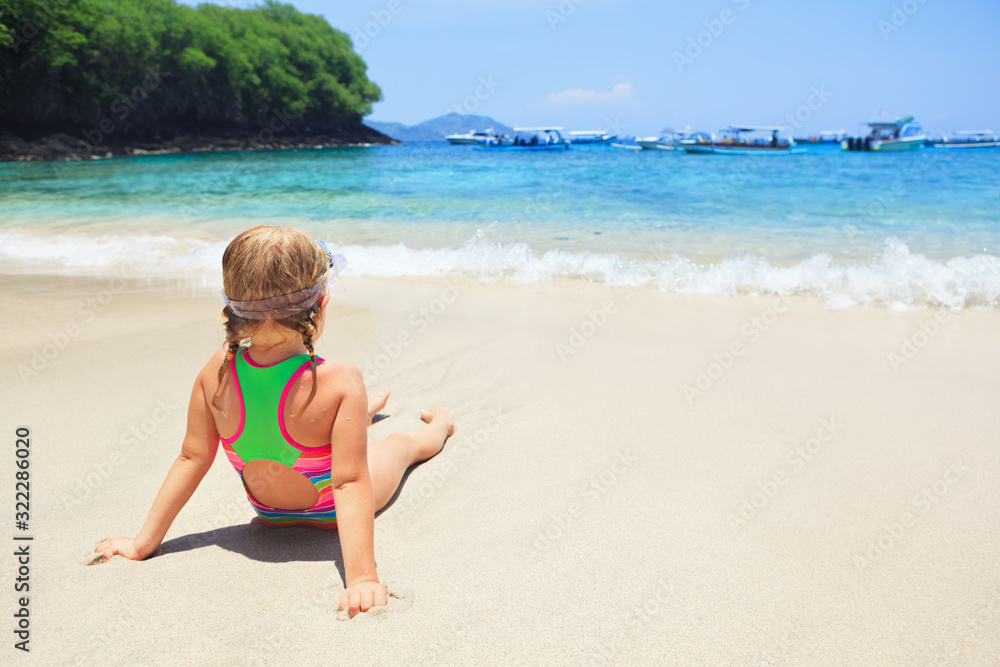 Happy family - active baby girl in snorkeling mask sit on white sand beach of tropical island. Look at scenic sea lagoon view. Travel adventure, swimming activity, watersport on summer cruise with kid Happy family - active baby girl in snorkeling mask sit on white sand beach of tropical island. Look at scenic sea lagoon view. Travel adventure, swimming activity, watersport on summer cruise with kid