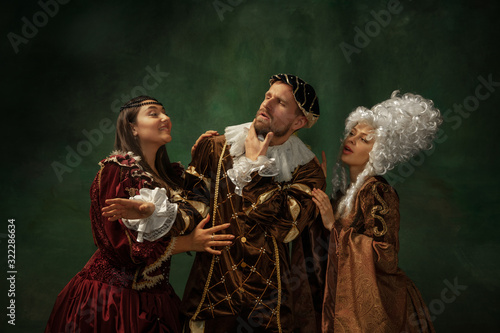 Love games pay attention. Portrait of medieval young people in vintage clothing on dark background. Models as a duke and duchess, princess, royal persons. Concept of comparison of eras, modern