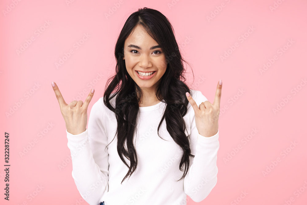 Image of young brunette asian woman smiling and gesturing horn fingers Image of young brunette asian woman smiling and gesturing horn fingers
