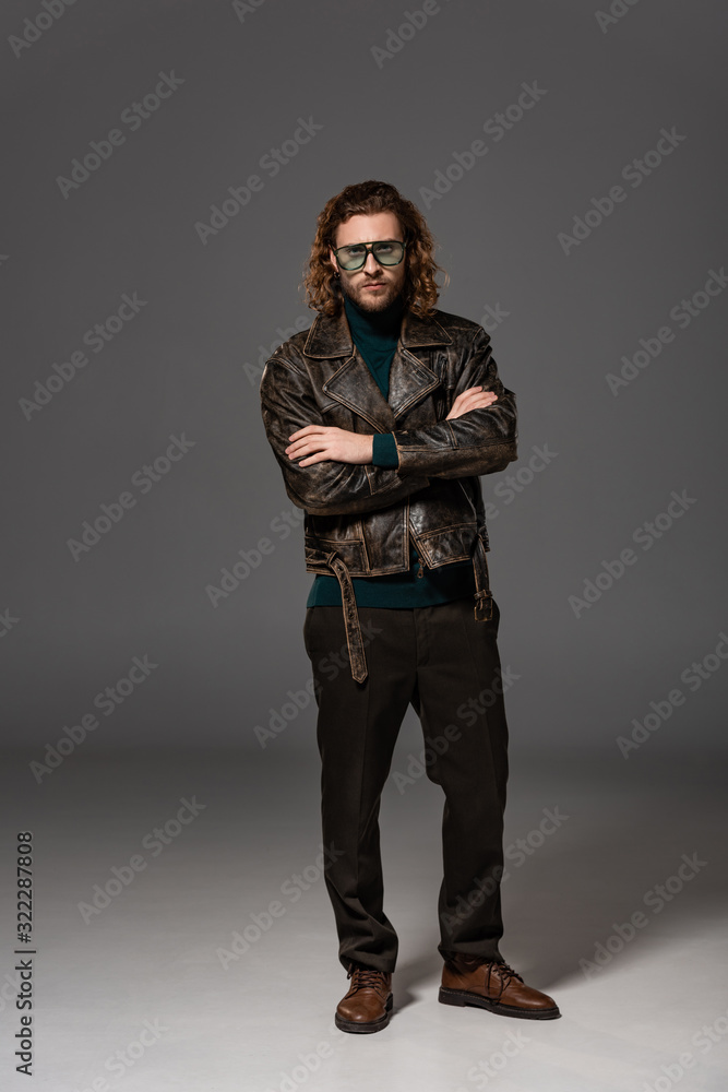 handsome man in leather jacket with crossed arms looking at camera on grey background