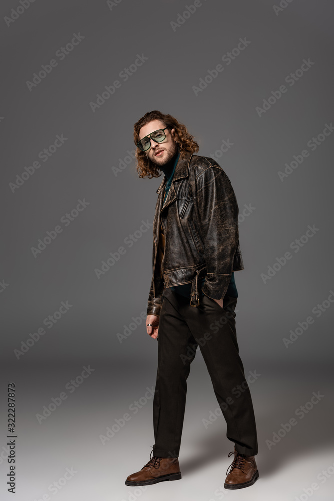 handsome man in leather jacket and trousers looking at camera on grey background handsome man in leather jacket and trousers looking at camera on grey background