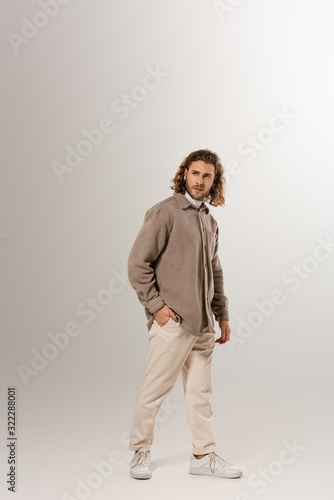 handsome man in shirt and trousers looking away on grey background