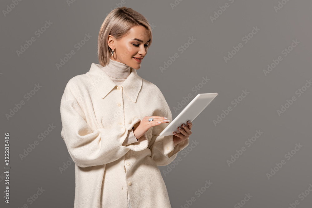attractive and smiling woman in white coat using digital tablet isolated on grey attractive and smiling woman in white coat using digital tablet isolated on grey
