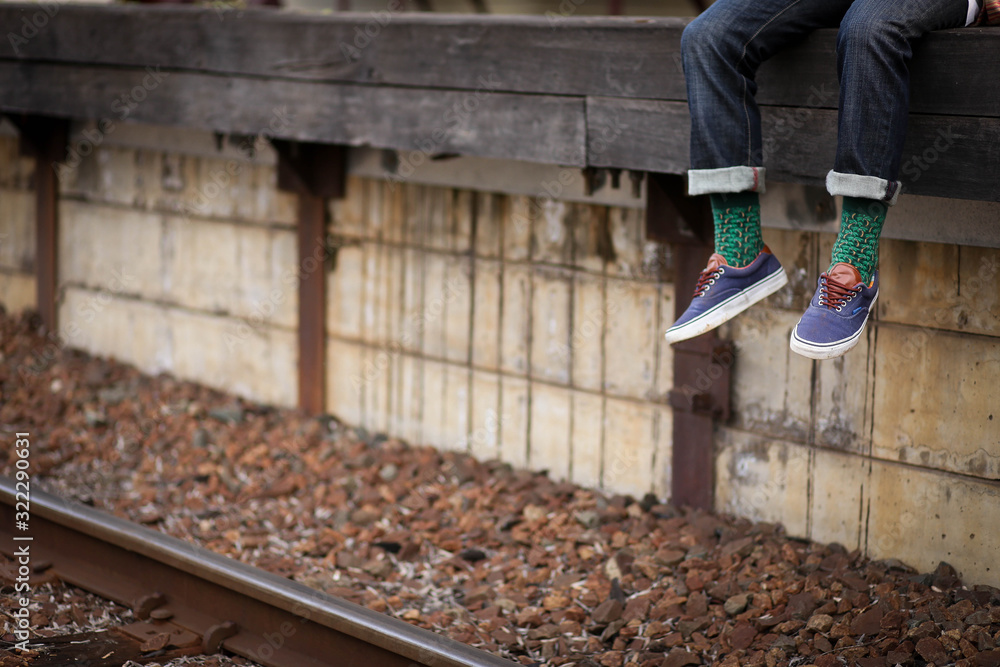 Feet dangling over train station platform wearing blue shoes with vibrant green socks Feet dangling over train station platform wearing blue shoes with vibrant green socks