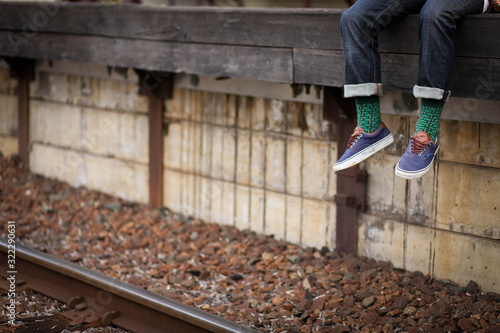 Feet dangling over train station platform wearing blue shoes with vibrant green socks