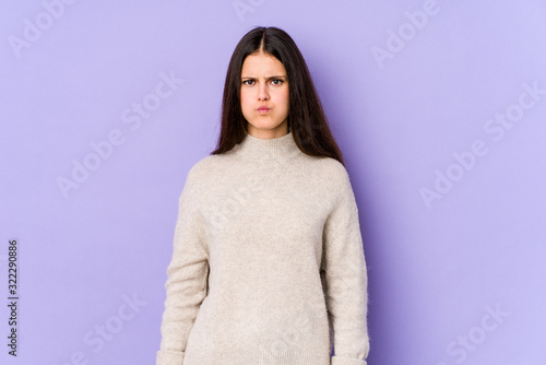 Young caucasian woman isolated on purple background blows cheeks, has tired expression. Facial expression concept.