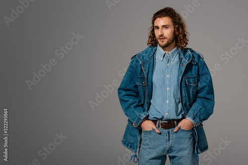 handsome and stylish man in denim jacket and jeans with hands in pockets isolated on grey © LIGHTFIELD STUDIOS