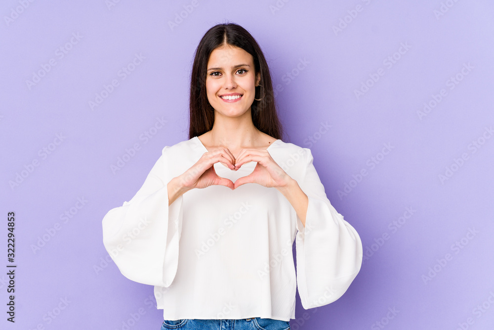 Young caucasian woman isolated on purple background smiling and showing a heart shape with hands. Young caucasian woman isolated on purple background smiling and showing a heart shape with hands.