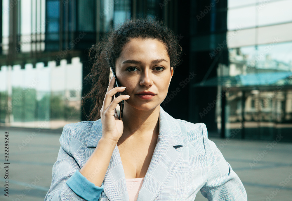 A young woman against the background of a business center is holding a mobile phone and talking.