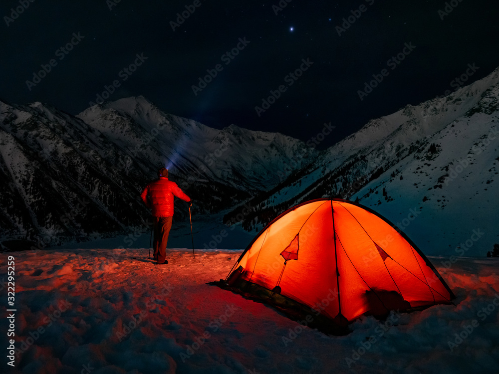 Overnight in the winter mountains. A tourist looks into the night starry sky. Red tent in the highlands