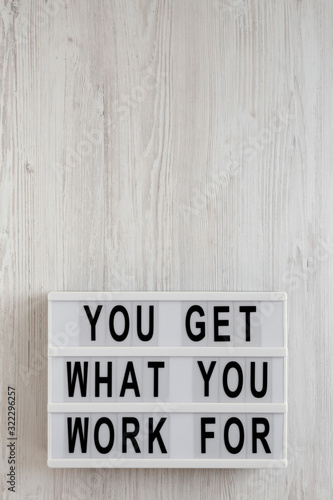 'You get what you work for' words on a modern board on a white wooden background, overhead view. Top view, from above, flat lay. Copy space.