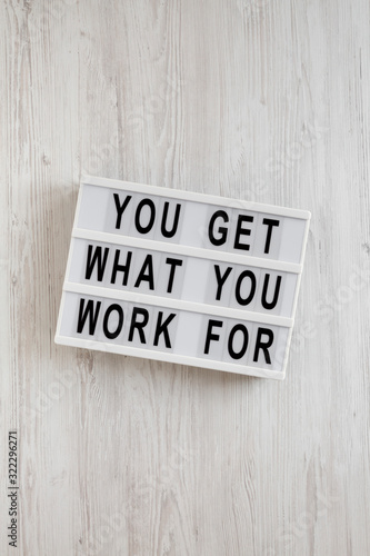 'You get what you work for' words on a lightbox on a white wooden background, overhead view. Top view, from above, flat lay.