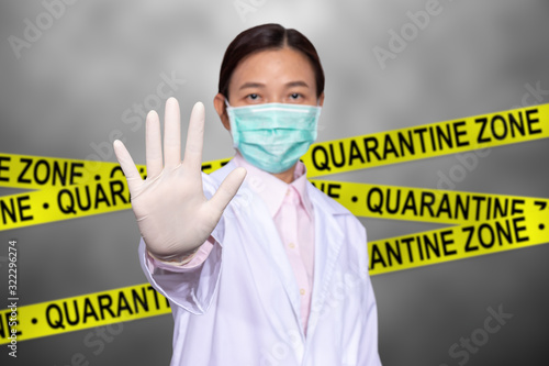Asian female doctor wear a medical mask, raise hand for stop sign to do not enter quarantine area with yellow quarantine sign on the back, entrance is forbidden in quarantine zone. photo