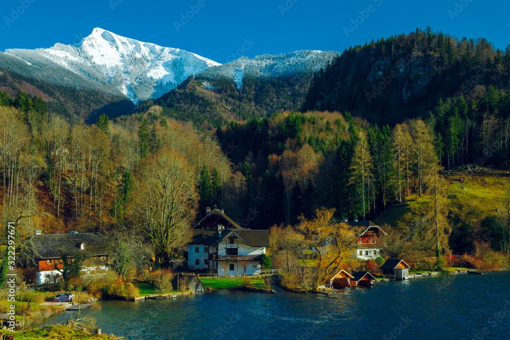 Fototapeta premium picturesque highland European village in Austria lake reservoir waterfront forest nature environment and Alps mountains snowy peak background scenic view