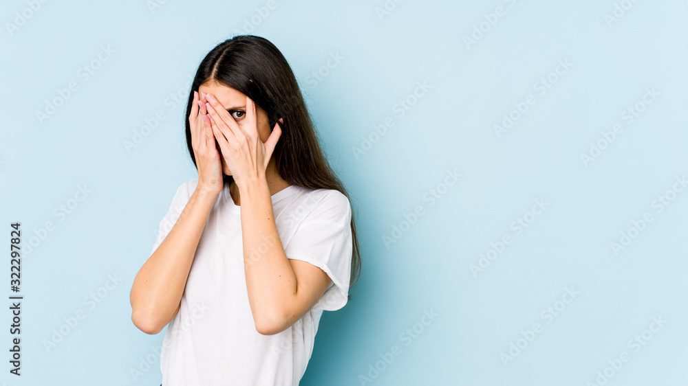 Young caucasian woman isolated on blue background blink through fingers frightened and nervous. Young caucasian woman isolated on blue background blink through fingers frightened and nervous.