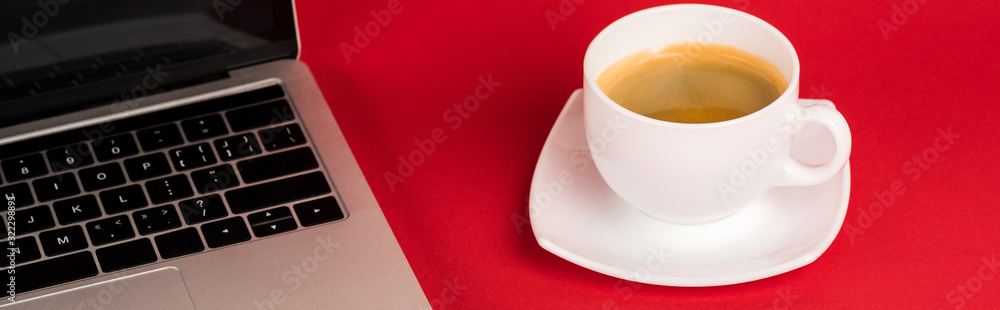 Panoramic shot of laptop with blank screen and coffee cup on red background