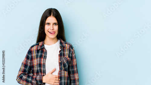 Young caucasian woman isolated on blue background touches tummy, smiles gently, eating and satisfaction concept. © Asier