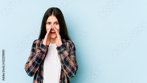 Young caucasian woman isolated on blue background saying a gossip, pointing to side reporting something.