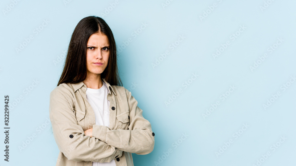 Young caucasian woman isolated on blue background frowning face in displeasure, keeps arms folded. Young caucasian woman isolated on blue background frowning face in displeasure, keeps arms folded.