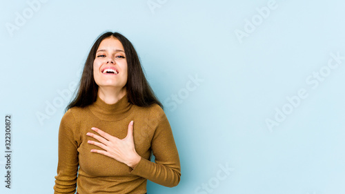 Young caucasian woman isolated on blue background laughs out loudly keeping hand on chest.