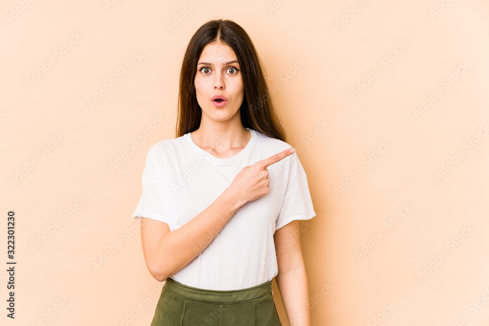 Young caucasian woman isolated on beige background pointing to the side Young caucasian woman isolated on beige background pointing to the side