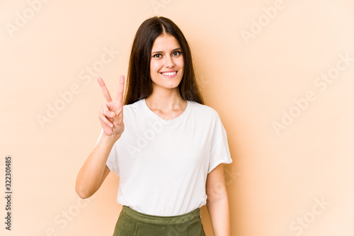 Wallpaper Mural Young caucasian woman isolated on beige background showing victory sign and smiling broadly. Torontodigital.ca