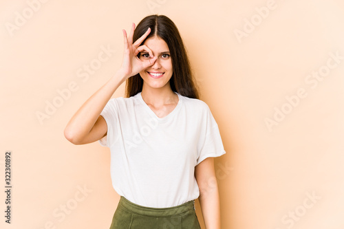 Young caucasian woman isolated on beige background excited keeping ok gesture on eye.