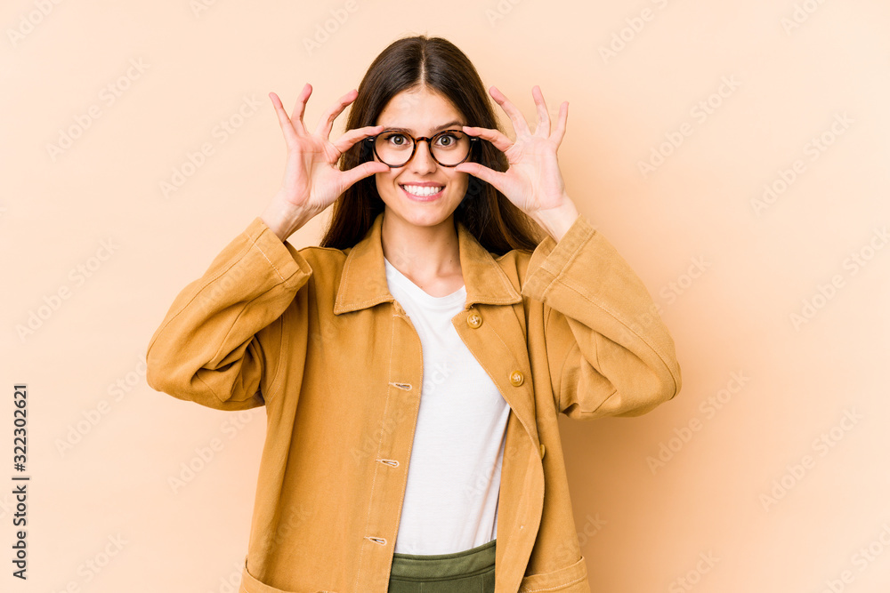Young caucasian woman isolated on beige background keeping eyes opened to find a success opportunity. Young caucasian woman isolated on beige background keeping eyes opened to find a success opportunity.