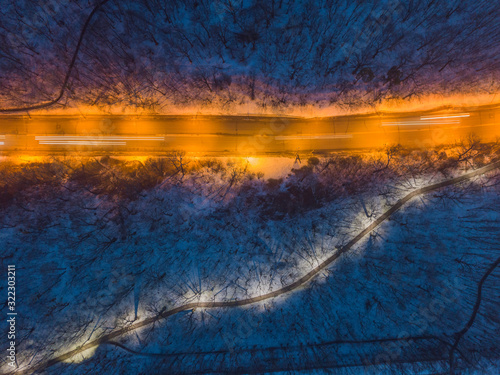 Aerial drone view. Illuminated road in a snowy park near the highway.