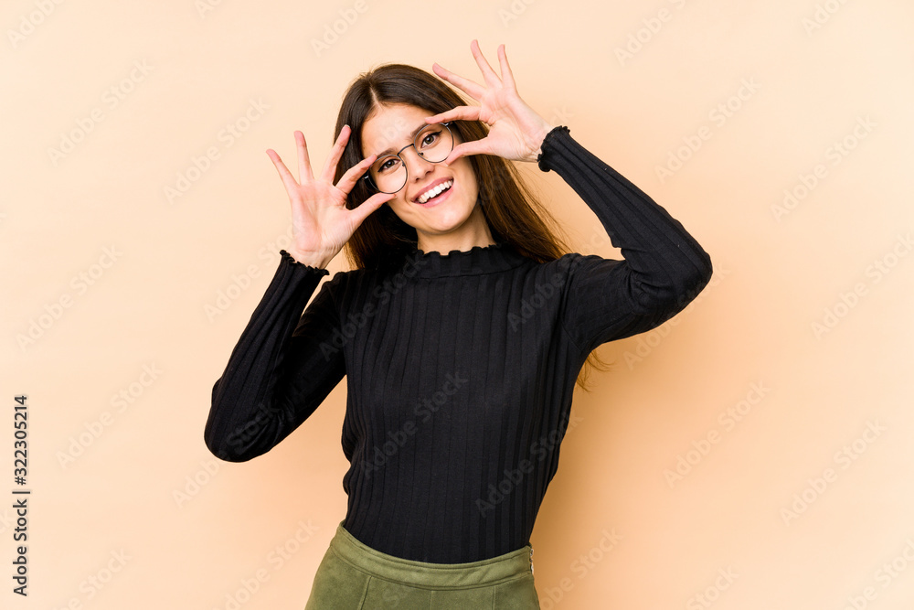 Young caucasian woman isolated on beige background showing okay sign over eyes Young caucasian woman isolated on beige background showing okay sign over eyes