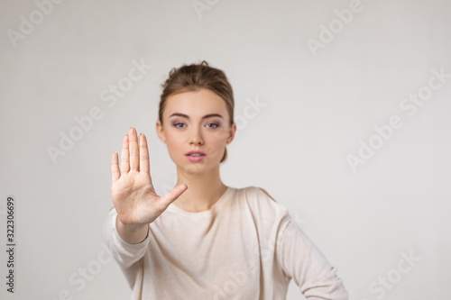 beautiful young woman making stop gesture on gray background.