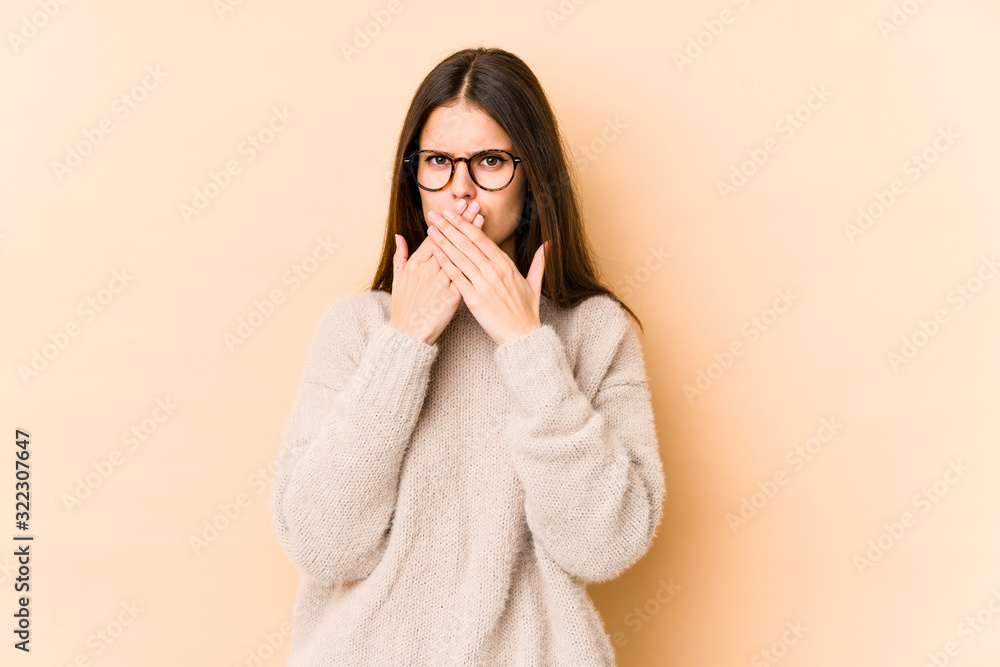 Young caucasian woman isolated on beige background covering mouth with hands looking worried. Young caucasian woman isolated on beige background covering mouth with hands looking worried.