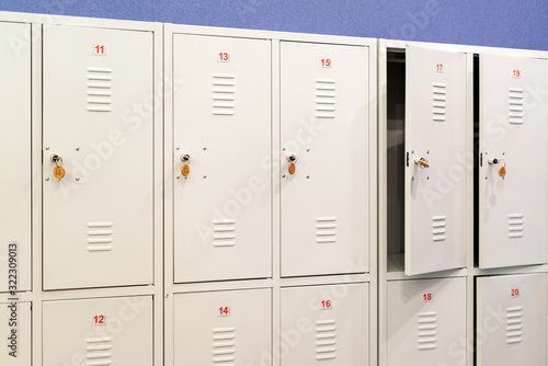 A row of grey metal school lockers with keys in the doors. Storage locker room in corridor of educational institution photo