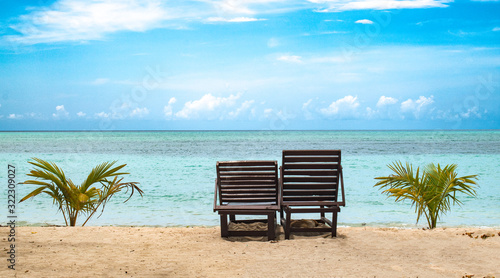 Photography Beautiful photo of two wooden recliner chairs lying vacant for tourists and honeymoon couples on beach for good times, amidst clear blue sky, calm ocean of turquoise color water and visible horizon