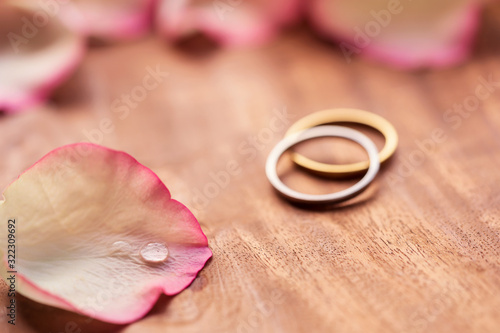 Romantic Wedding Card Background. Wedding rings beautifully blurred in background with pink rose petals with copy space. Concept for valentine's day, propose, anniversary, wedding card, pamphlet.