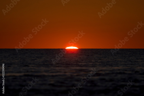 The beginning of a sunrise over the ocean with the sun just peeking over the calm water horizon.