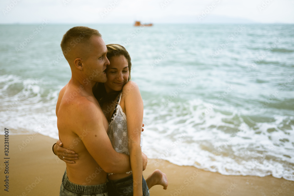 Fototapeta premium Beautiful guy and girl run and enjoy on the beach on the ocean or sea. Honeymoon in the tropics of a husband and wife. Romance in hot countries. Wallow in the sand and be happy and in love. Lovers