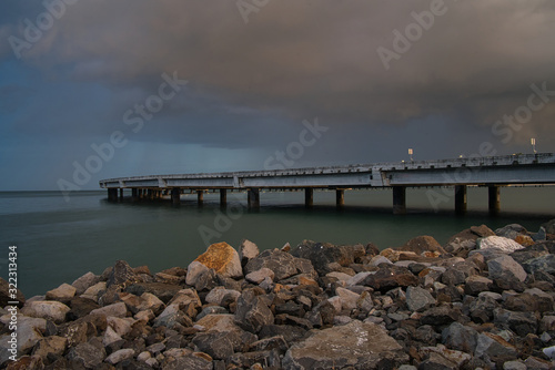 Eine menschenleere Brücke über das Meer in Panama, Steine im Vordergrund und lila Wolken, kurz vor einem Gewitter