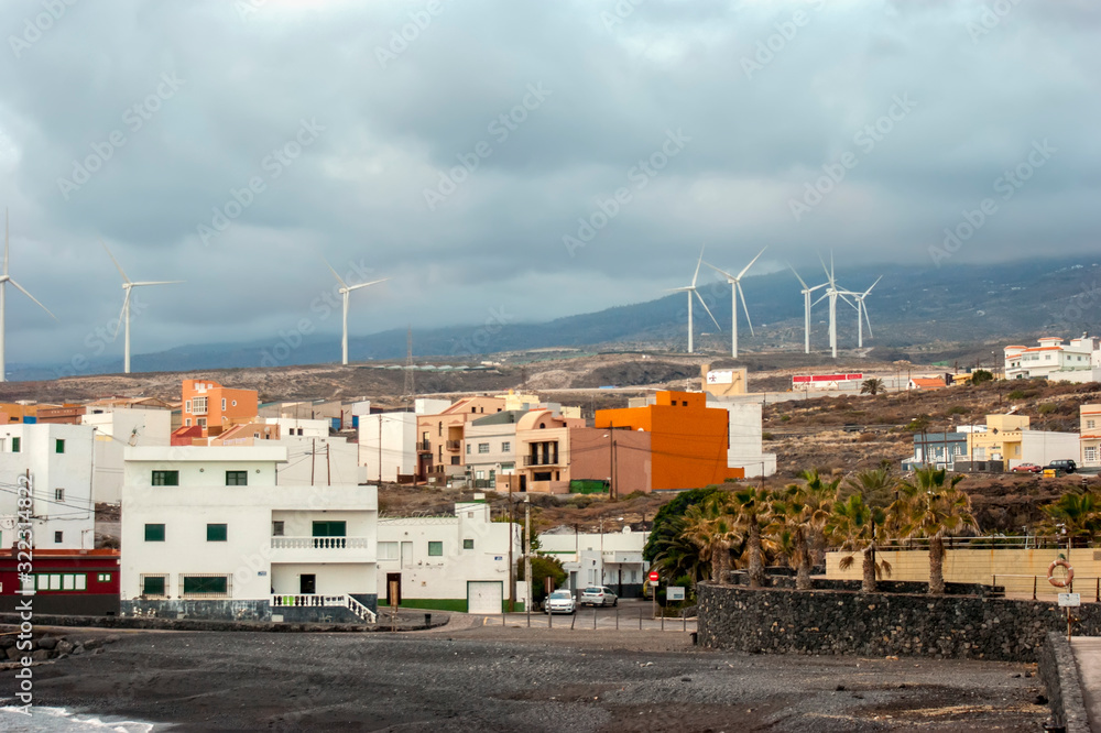 Small coastal town of Las eras at sunset. Concrete houses that look like boxes. In the distance, you can see wind turbines-alternative energy sources. 