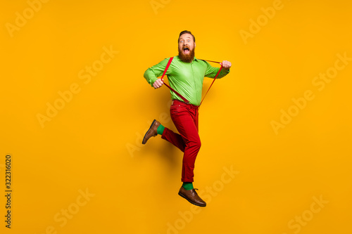 Full length photo of careless childish crazy funky man jump pull his modern suspenders scream feel rejoice wear stylish outfit shoes isolated over yellow color background