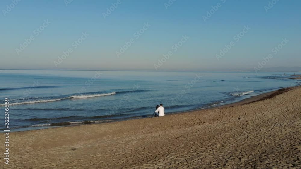 young couple sitting on the beach by the sea. Enjoy the beauty of the sea and sunrise. Aerial view young couple sitting on the beach by the sea. Enjoy the beauty of the sea and sunrise. Aerial view