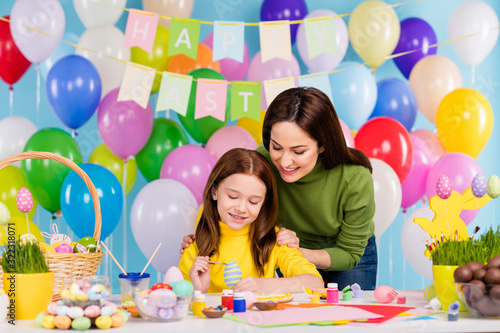 Portrait of nice attractive lovely cute careful creative cheerful cheery girls preparing making festal handmade decor April day bright vivid shine vibrant blue color background