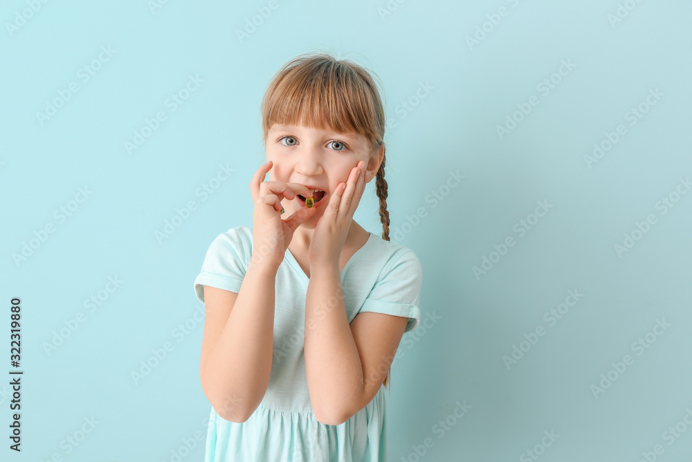 Little girl taking fish oil pill against color background Little girl taking fish oil pill against color background