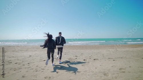 Young couple in love holding hands running towards the sea, playful having fun on beach holiday. Young trendy man and woman, people on sand beach photo