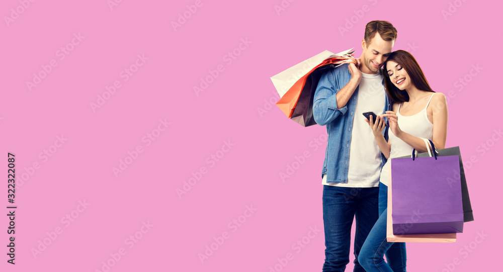 Love, holiday sales, shop, retail, consumer concept - happy couple with shopping bags, looking at mobile phone, standing close to each other. Over rose pink color background.
