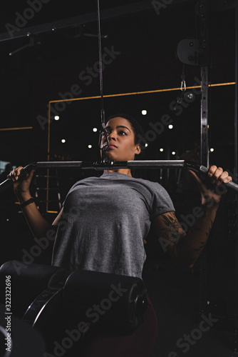 selective focus of african american girl with tattoo training on gym machine