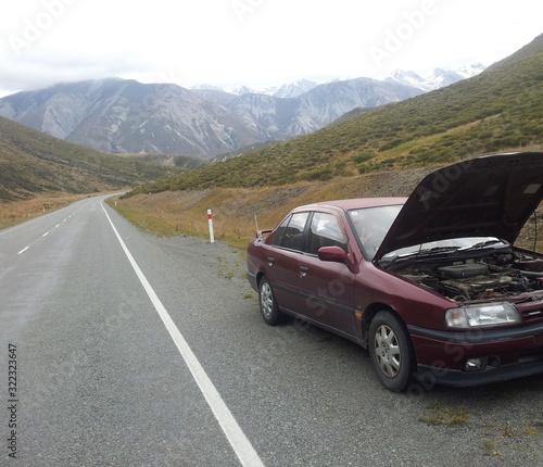 Car breakdown on the side of the empty road, mountains in the background